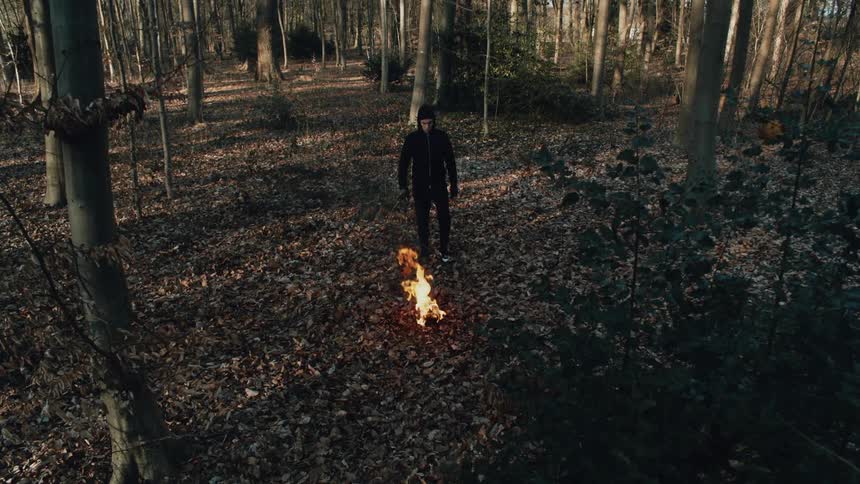 A man walks towards a small fire burning in a forest