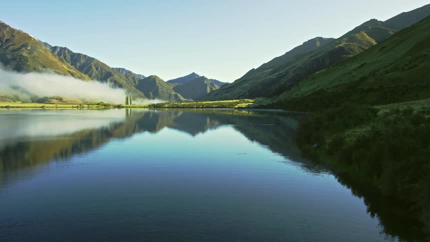 Person stand on shore fishing in water reflecting the mountains and the sky