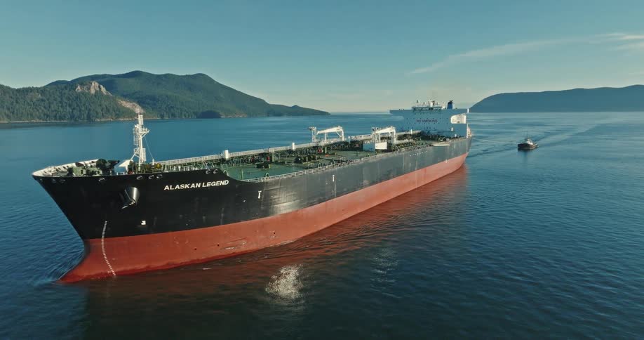 A cargo ship pulls a small boat behind it in the ocean