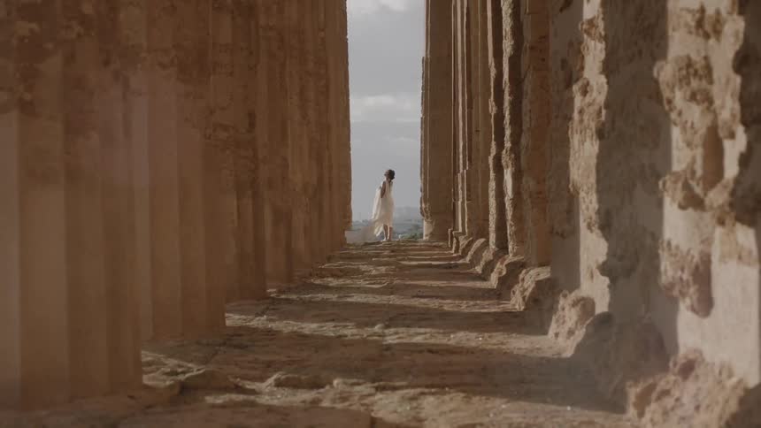 A woman is standing among pillars in the distance