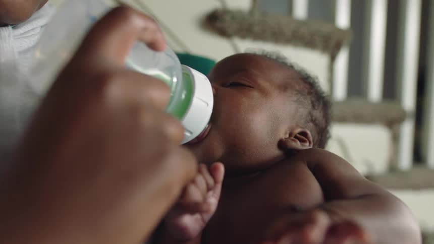 A woman feeds her baby a bottle while sitting on the stairs at home