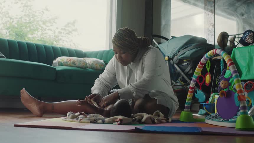 A woman changes the diaper of a baby while sitting on the floor of a living room during the day