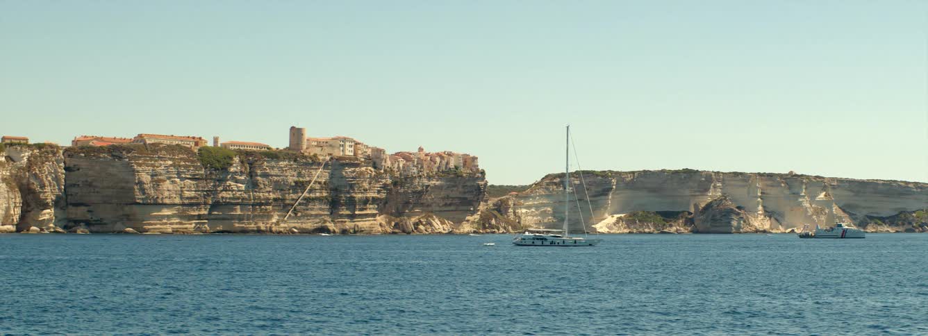 Bonifacio, Corsica: A landscape of buildings standing on the of coastal cliff and sailboat sailing on water