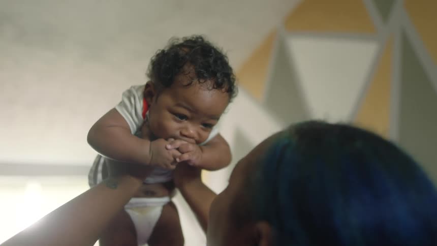 Mother holds newborn baby up and kisses his forehead