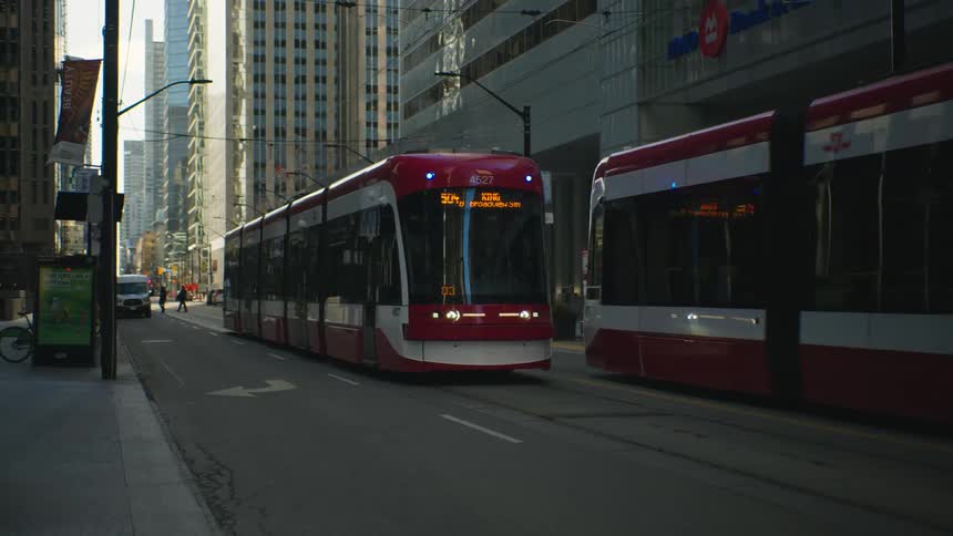 Two buses cross paths on a downtown street with tall buildings and pedestrians crossing the road