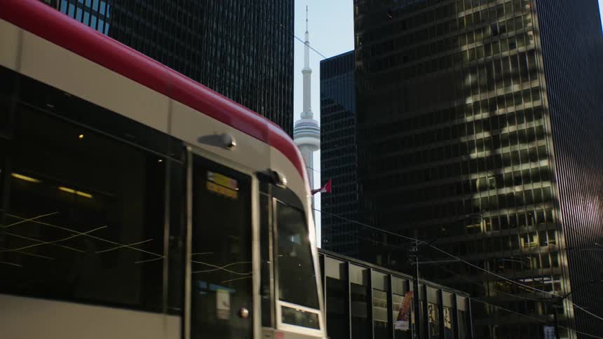 Two buses cross paths on a downtown street as a tower with a tall spire is seen between tall buildings