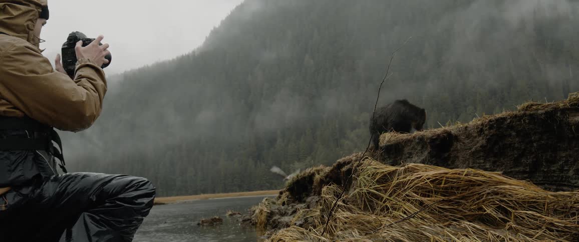 A man photographs a bear by the water