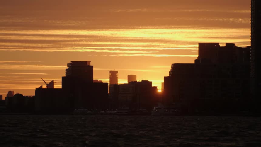 The silhouette of coastal city buildings and wind turbine against a golden sky