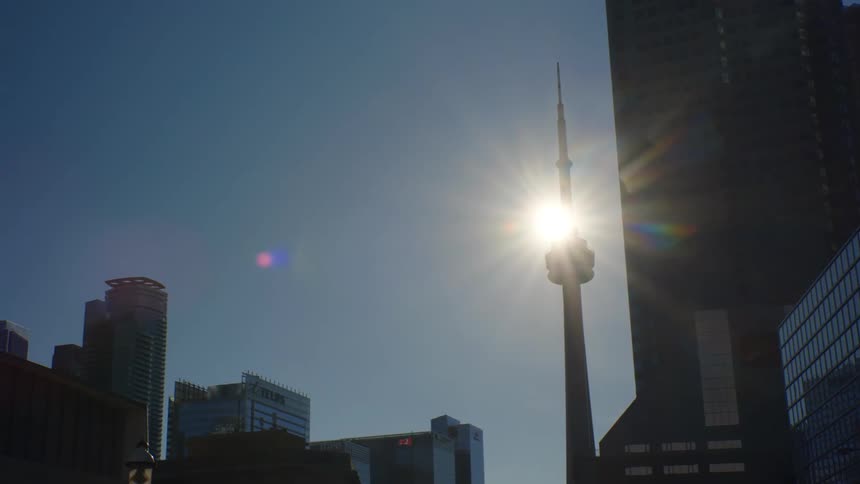 Sun shines behind the silhouette of the cn tower in the toronto skyline