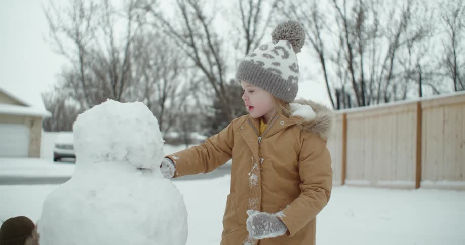 A girl smoothes out a snowman shes building at the end of her driveway