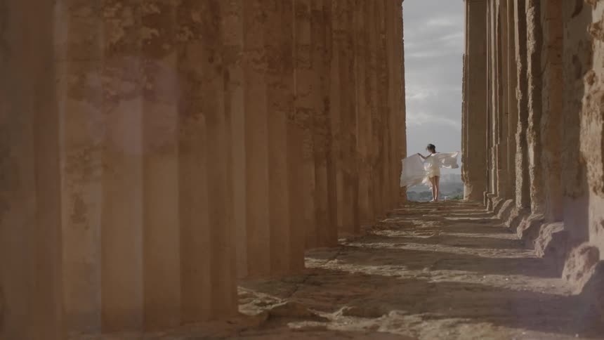 A woman allowing the breeze to lift the train of her dress while she visits the acropolis