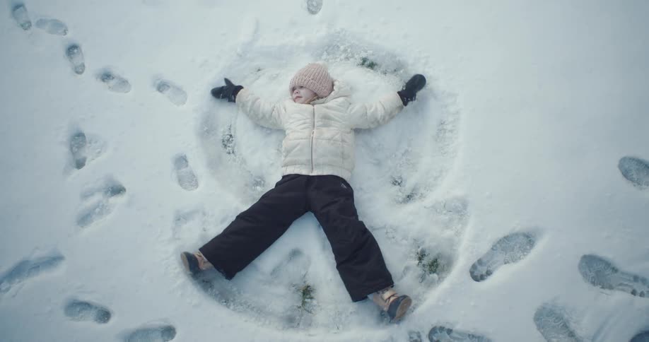 A little girl lying in the snow making a snow angel