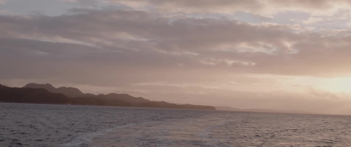 The silhouette of mountain peaks and sun shining through clouds onto the choppy water surface