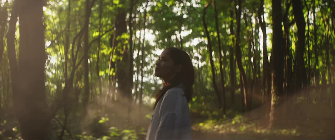 A woman is looking around he forest
