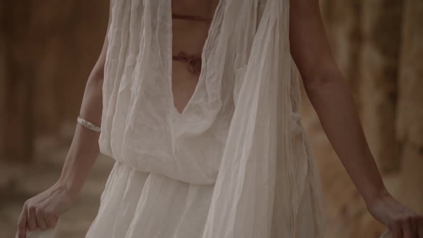 A woman wearing white walks slowly holding sides of dress