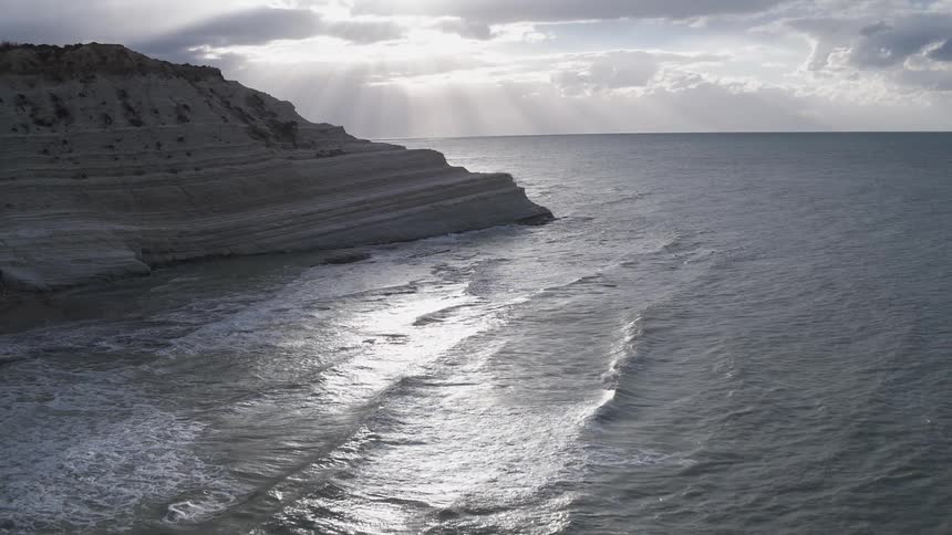 Sun shines through the clouds hitting the water behind a rock formation