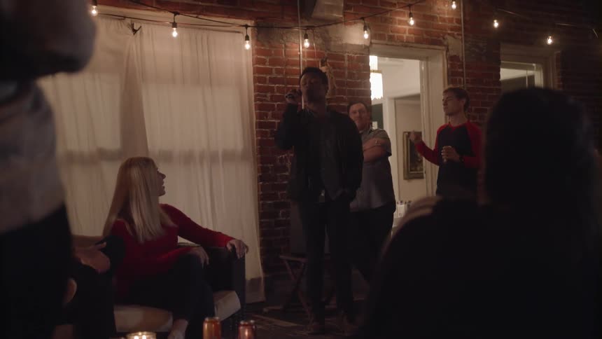 A man sings on a patio at a home while his friends watch and share drinks