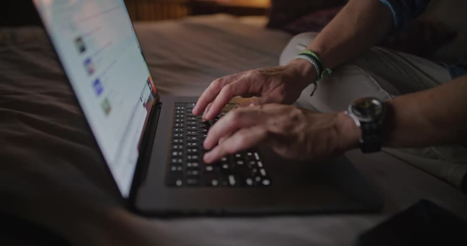 Man sitting on bed types on laptop