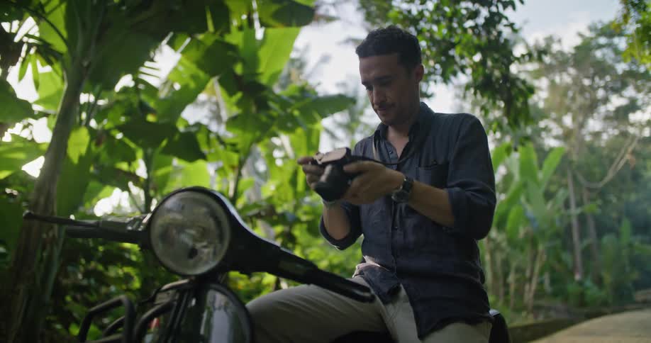 A man takes photos while sitting on his motorcycle in a jungle