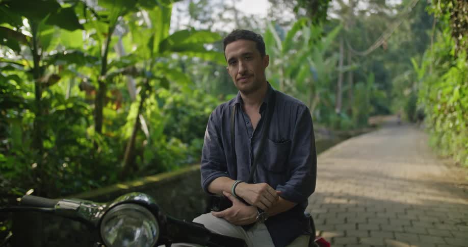 A man poses on a motorcycle while sitting on a cobblestone road in the jungle