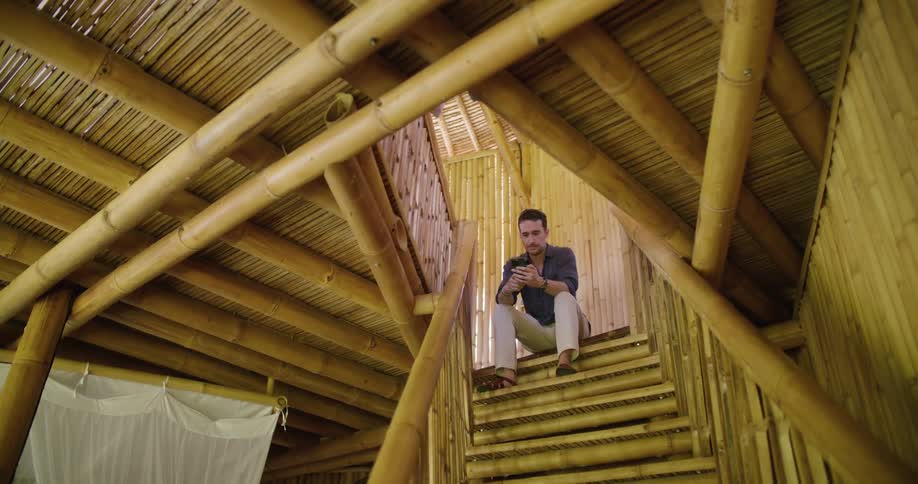 A man using his smartphone while sitting at the top of indoor stairs