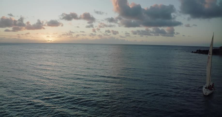 Aerial view of a sailboat sailing on the ocean near the coast at sunset