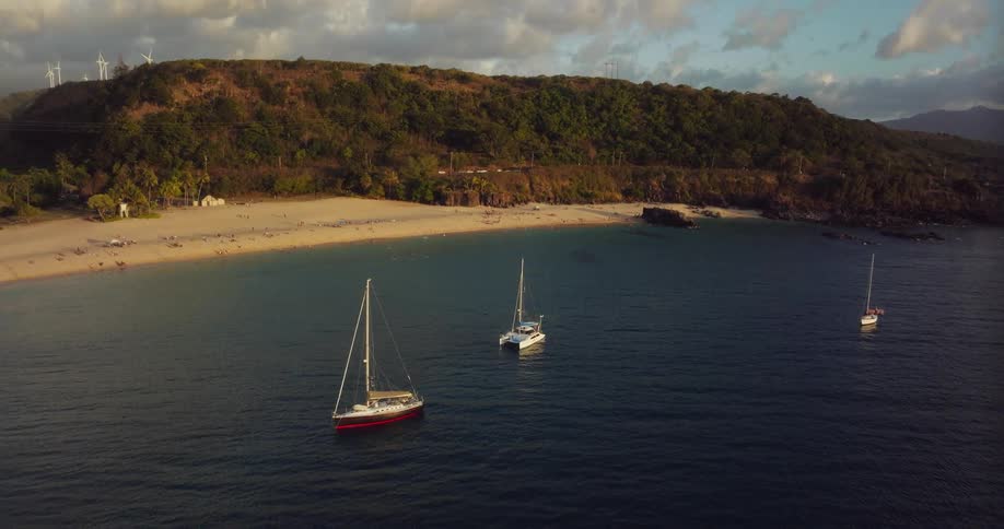 People party on boats sailing just off the shore of a secluded beach