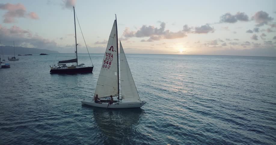 A sailboat sails the ocean near the coast in the evening