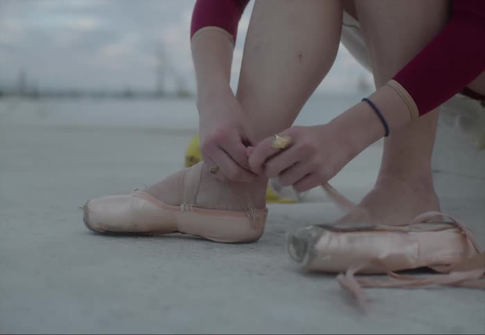 Ballerina sitting on the floor ties the laces of her toe shoes outdoors