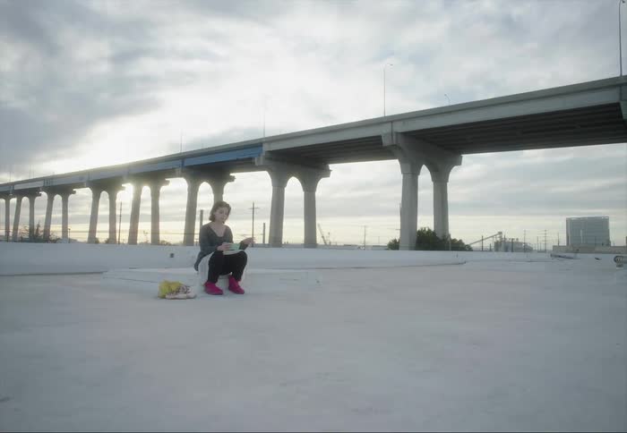 Woman sits gesturing while reading with elevated highway in the background