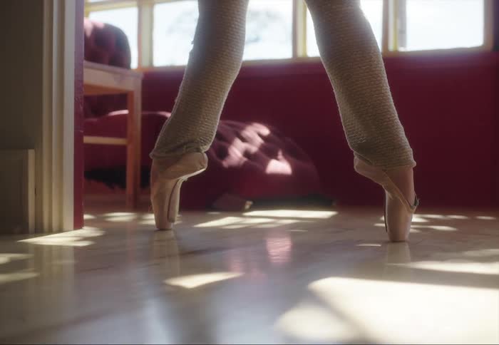 Ballerina moves onto her toes on hardwood floor near windows