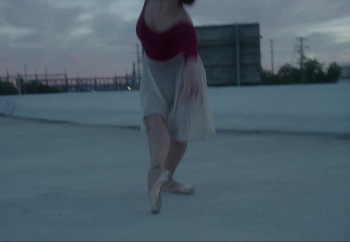Young ballerina dancing on the roof of a building close to a bridge at evening