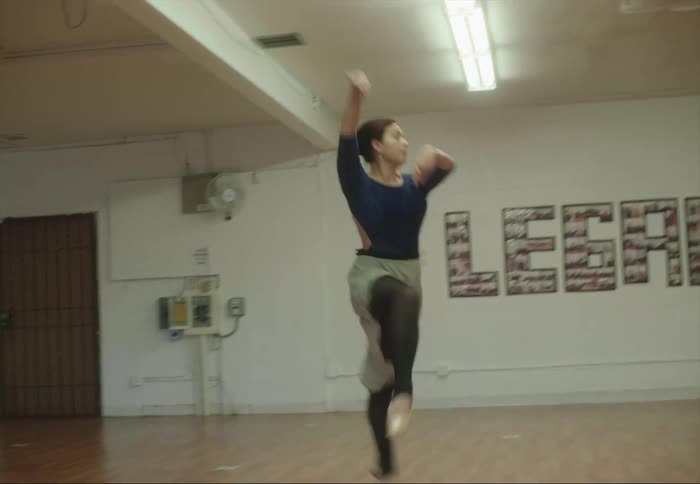 A woman is leaping as she dances across the floor