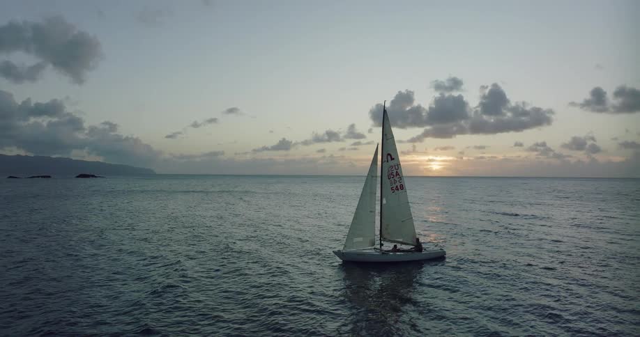 Aerial view of white sailboat sailing on ocean water at sunset