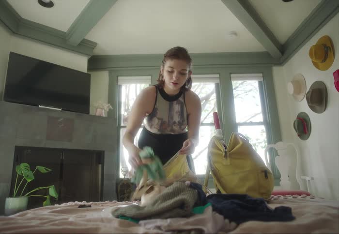 Young woman packing clothes on bags over the bed at home