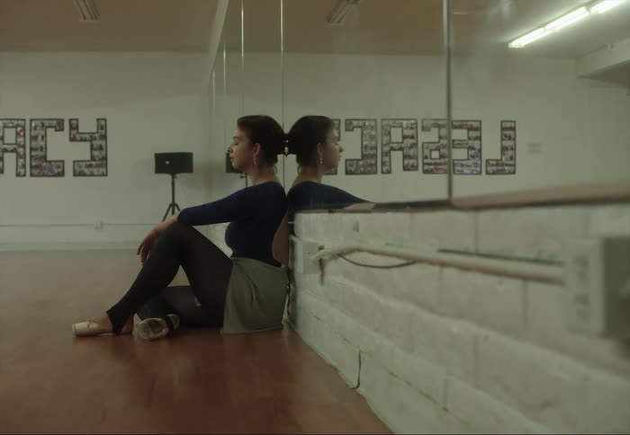 A woman rests while sitting against the wall in a dance studio