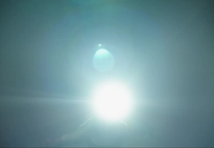 A woman is dancing and moving her arms and bends down as a light shines brightly behind her and everything goes dark
