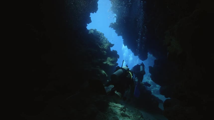 Two divers swim through a small opening in a cave