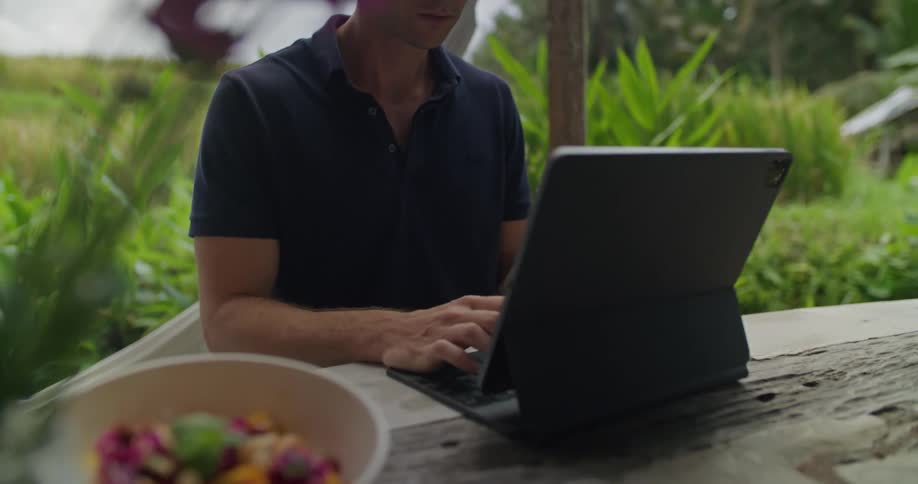 Man sitting at outdoor picnic table near field types on laptop