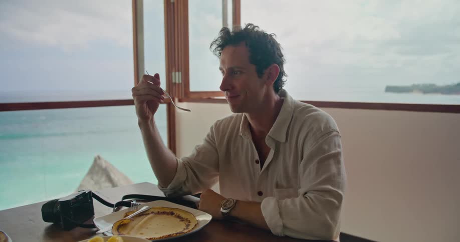 Man eating lunch on the table while talking to someone on an apartment near the ocean