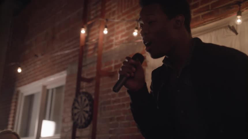 Young man sings karaoke into a microphone in front of friends at a party