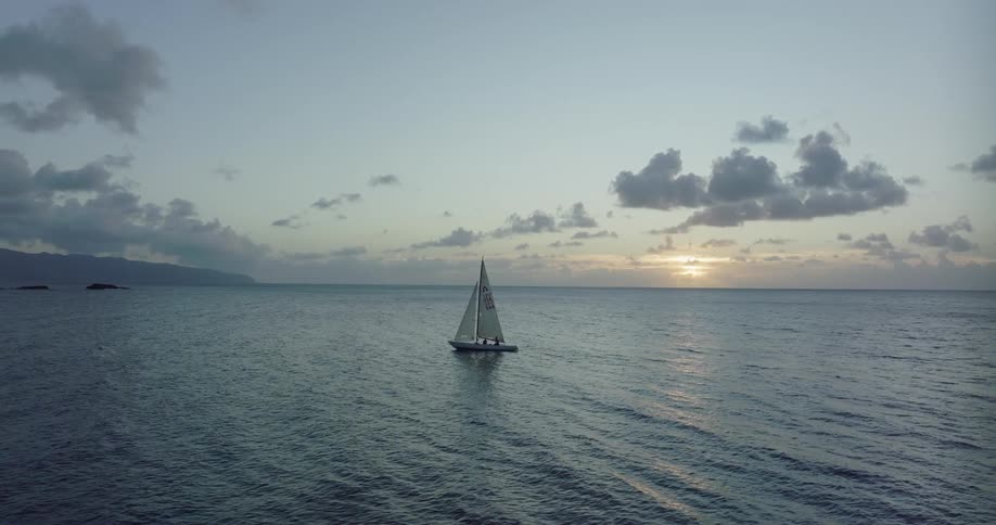 Aerial view of a small sailboat on the calm surface of the ocean at sunset
