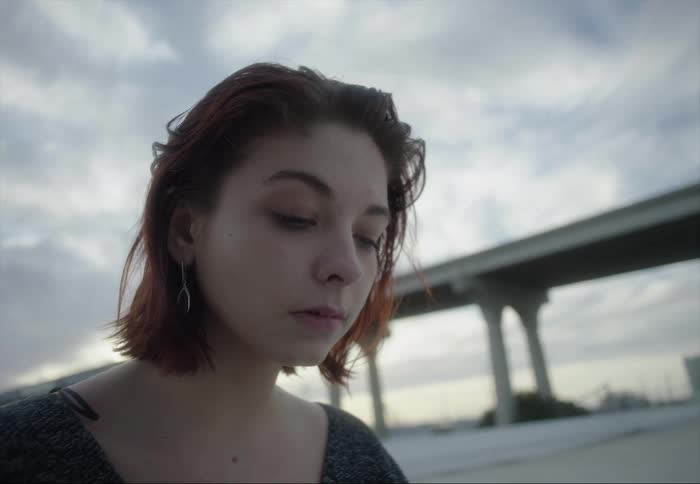 Close up of the face of a beautiful young woman sitting on the roof of a building near a bridge at sunset
