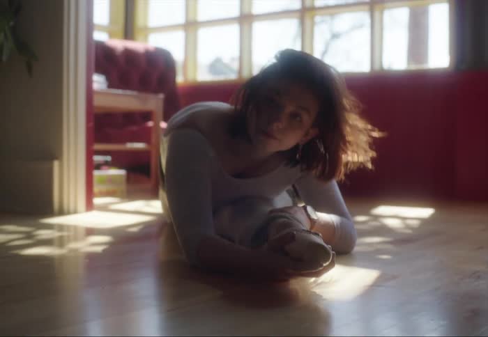 Young female ballet dancer stretches on the floor of the living room looking at the camera