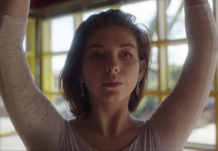 Woman in room with walls of windows raises her hands over her head