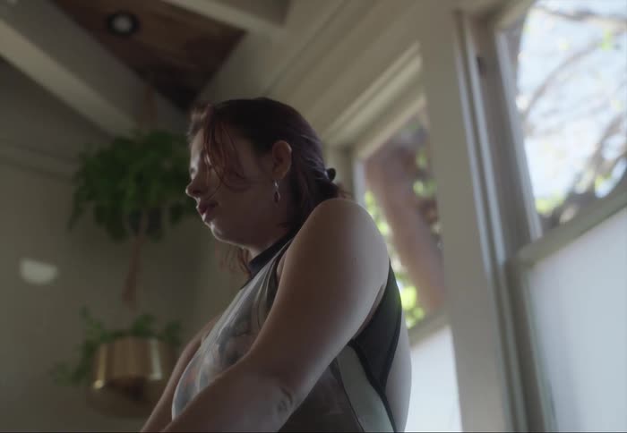 A woman sits down indoors and takes a deep breath with her eyes closed