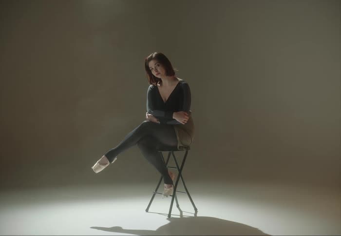 A woman wearing ballet shoes sitting on a stool posing for a photograph