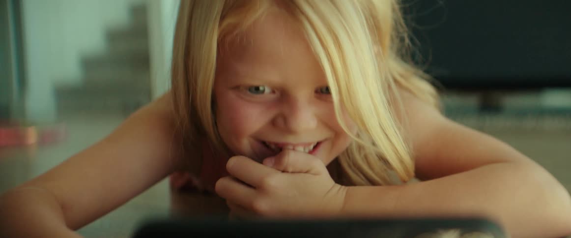 A girl happily watches a computer tablet while lying on the floor