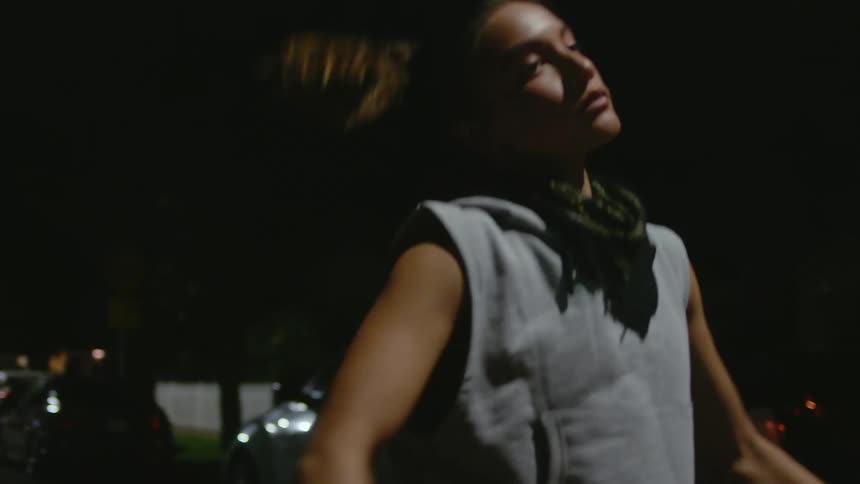 Woman jogs along road past parked cars at night