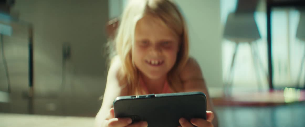 A girl entertains herself with a computer tablet while lying on the floor